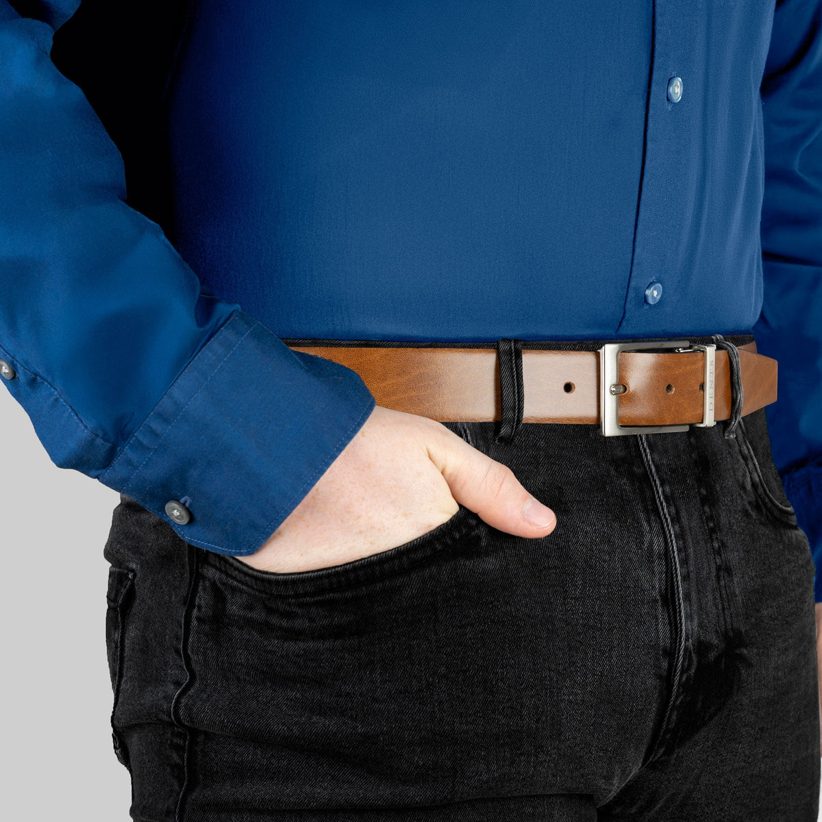 Men’s heritage reversible full-grain leather belt with satin nickel buckle in black/tan, hand in pocket.
