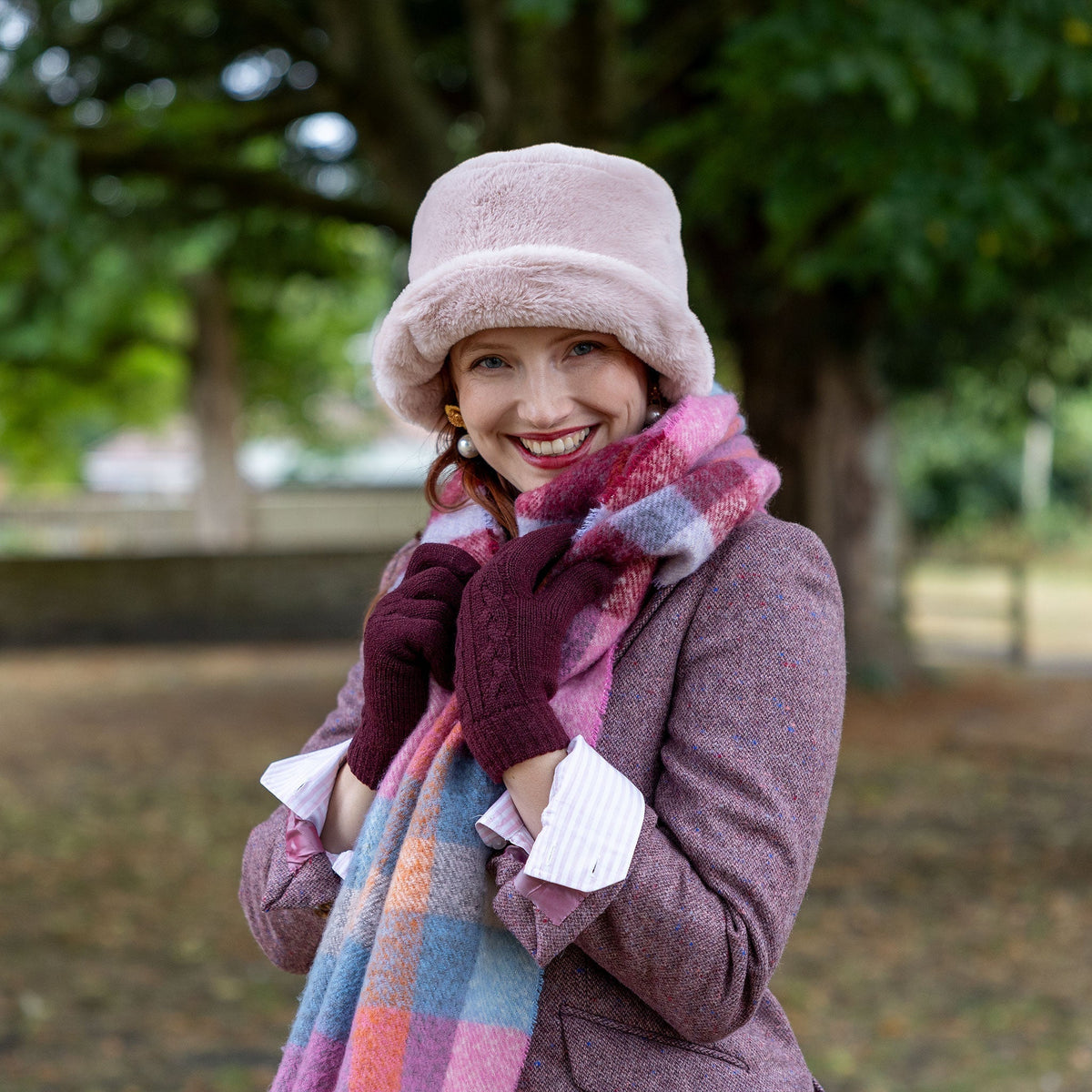 Close up of woman wearing cable knit gloves in purple, with a pink scarf and pink suit outside.