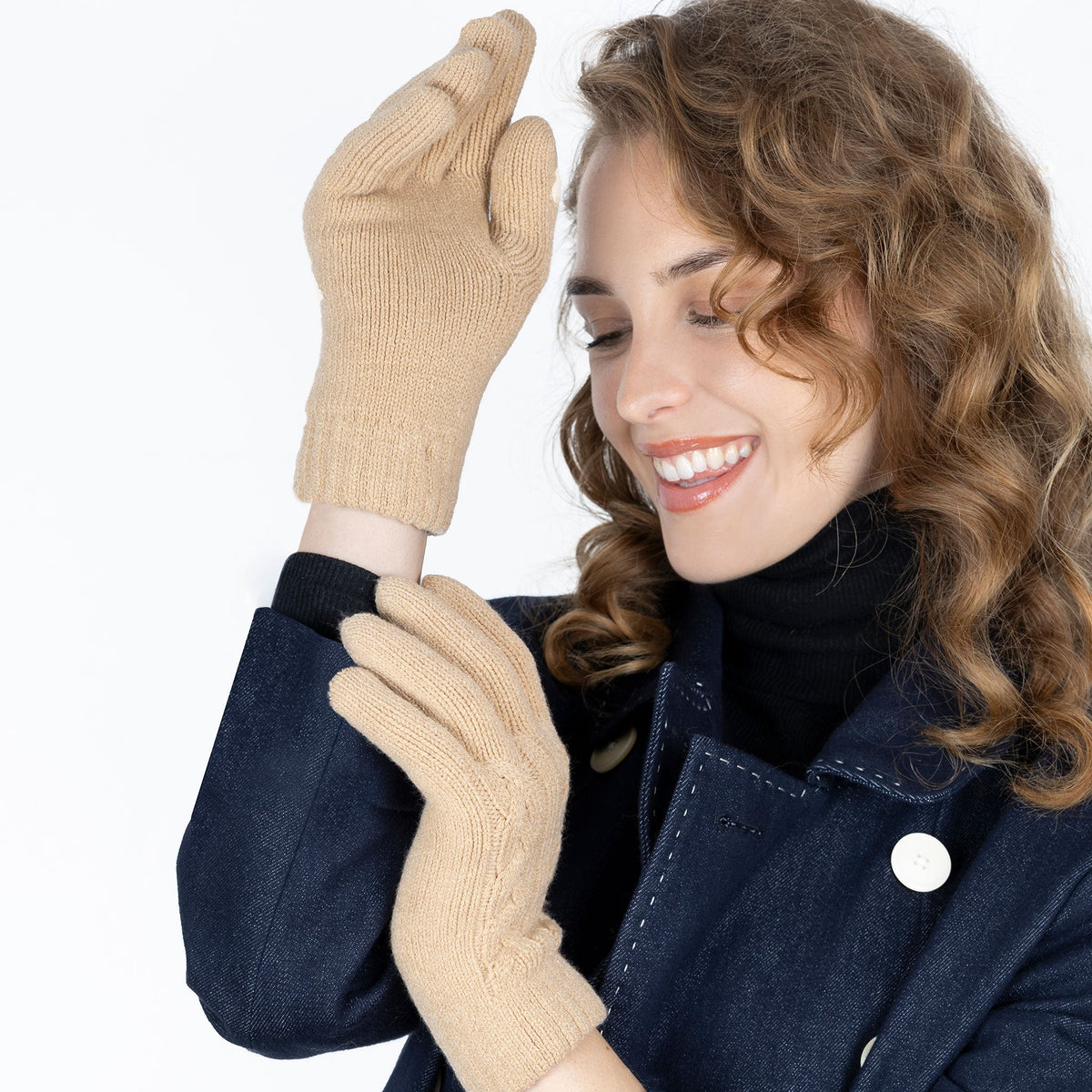 Woman wearing cable knit gloves in beige, with white background in the studio.