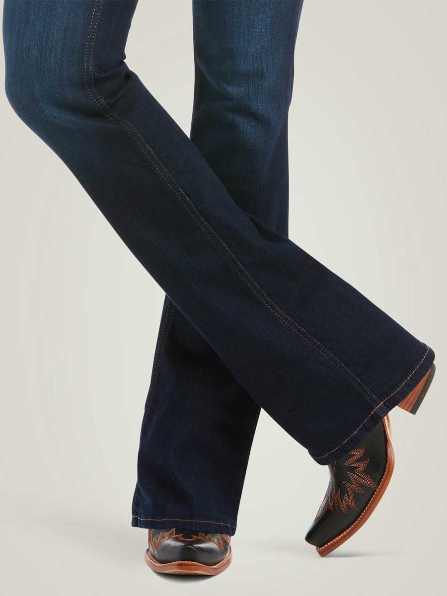 Dark blue jeans worn with brown cowboy boots on a light gray background
