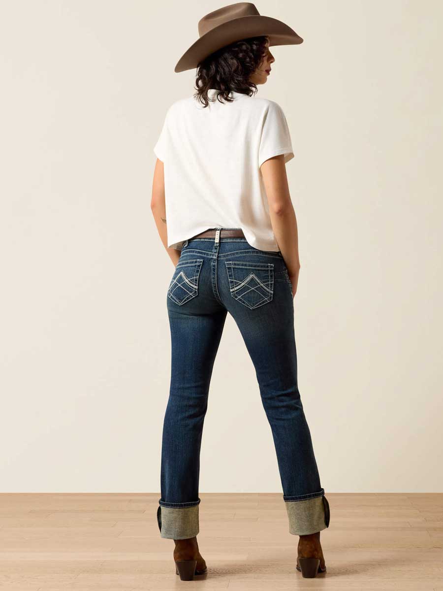 Person wearing blue jeans and a white shirt with a brown hat, standing against a plain background.