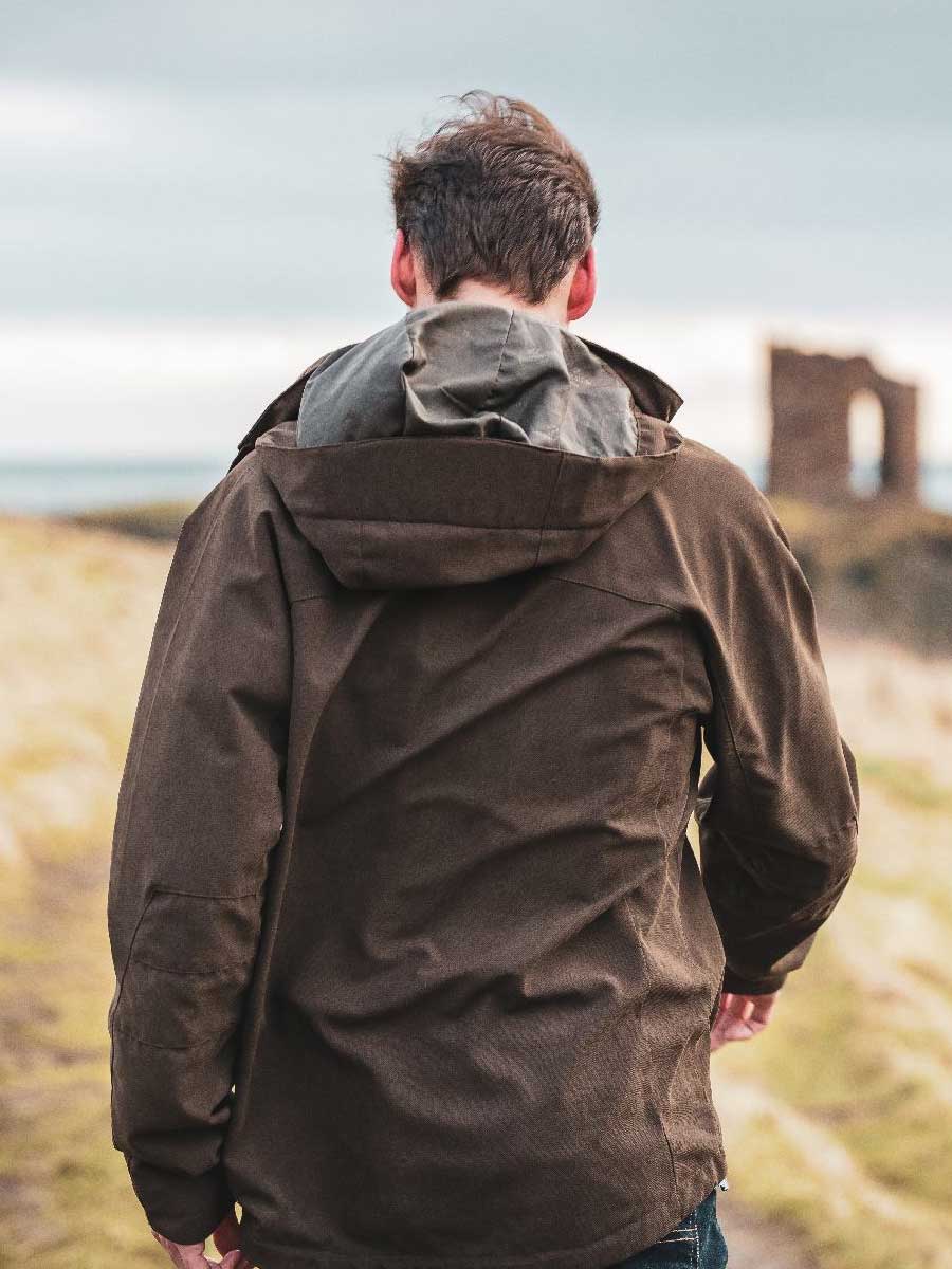 Person wearing a brown jacket standing in a scenic outdoor setting with ruins in the background.