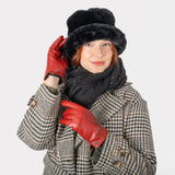 Woman wearing touchscreen single point faux fur lined leather gloves in red, in a check coat and black hat and scarf. With white background.