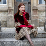Woman wearing burgundy satin below elbow gloves in burgundy dress on stone steps. 