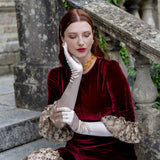 Woman wearing light pink satin below elbow gloves in burgundy dress on a stone steps. 