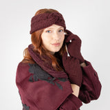 Woman wearing cable knit gloves in burgundy, in burgundy coat and matching scarf and headband. 
