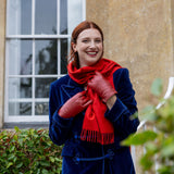Woman wearing touchscreen single point faux fur lined leather gloves in red, in a blue coat and red scarf outside.