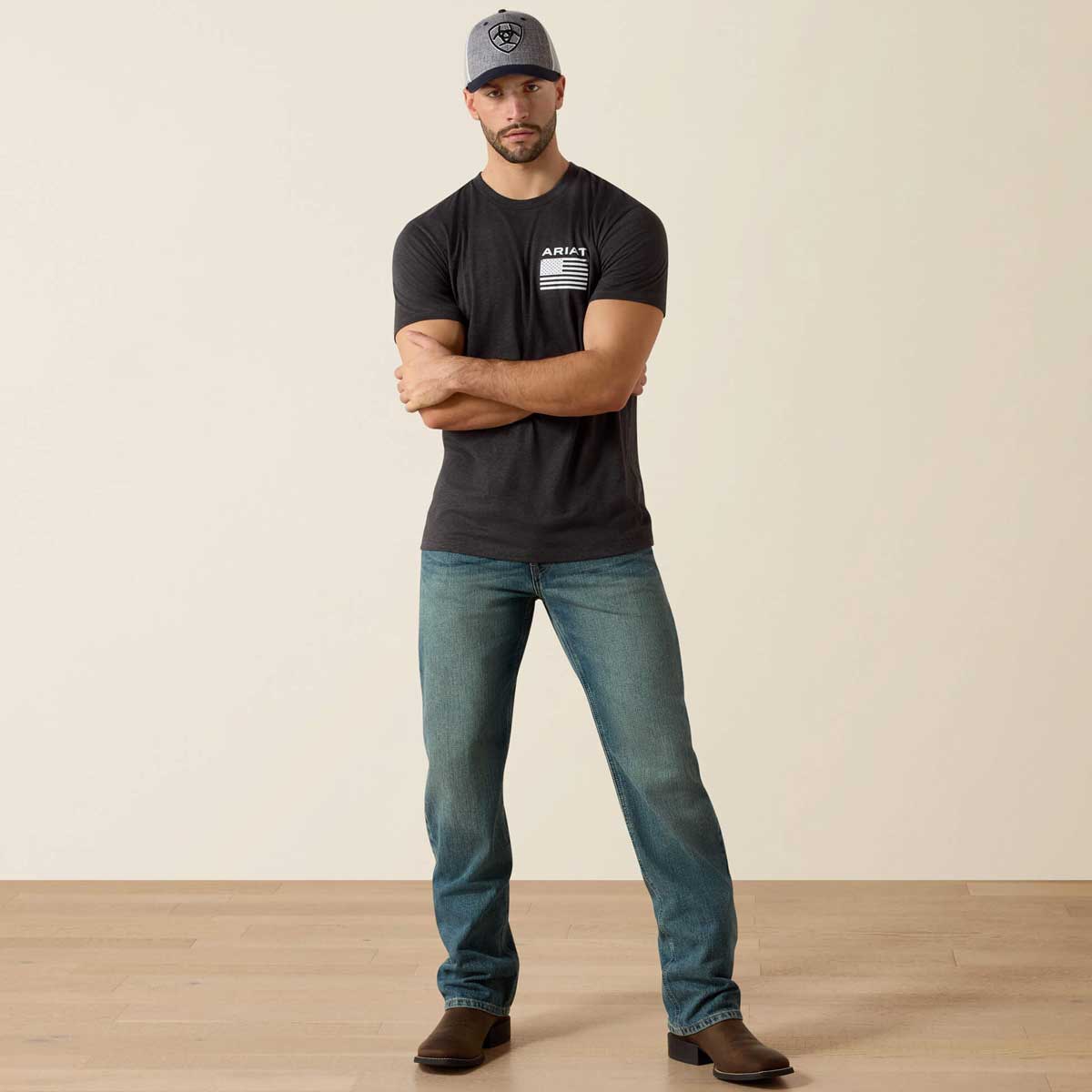 Man wearing a black t-shirt with a logo and blue jeans standing against a plain background