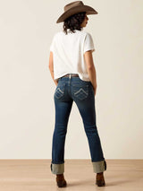 Person wearing blue jeans and a white shirt with a brown hat, standing against a plain background.