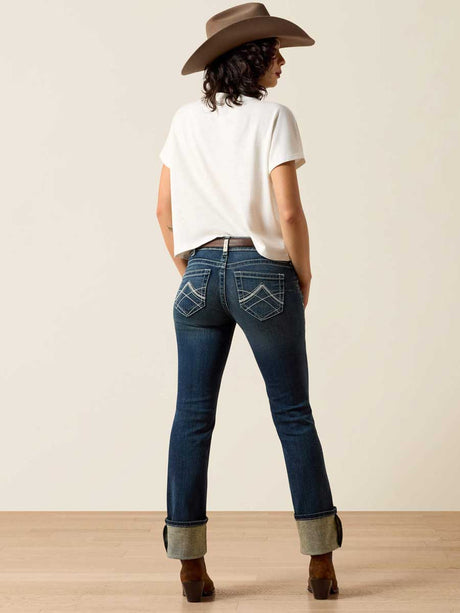 Person wearing blue jeans and a white shirt with a brown hat, standing against a plain background.