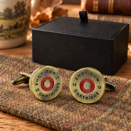 Antique brass-tone and red cartridge cap cufflinks on country tweed beside Farley's black presentation box