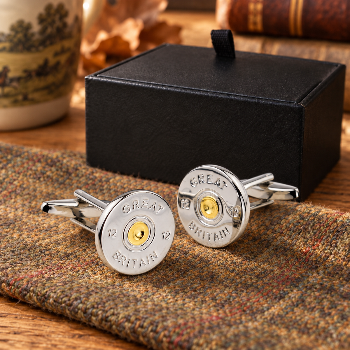 Farley's Great Britain silver and gold cartridge-cap cufflinks on tweed beside the black presentation box