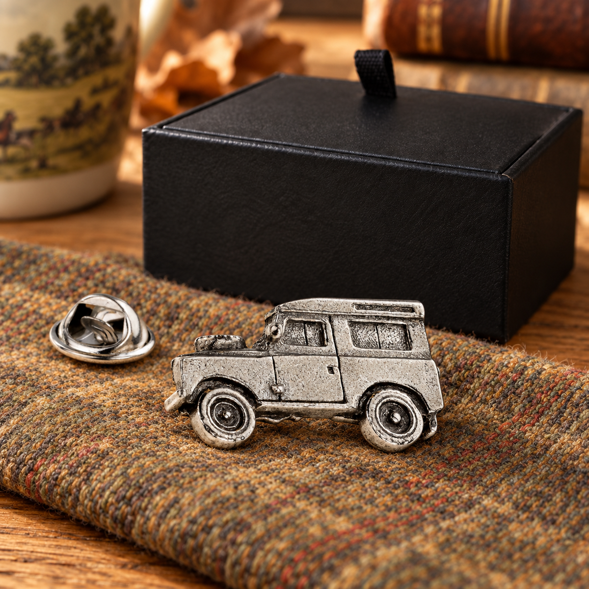 Farley's Land Rover Defender pewter lapel pin badge on tweed beside the black presentation box