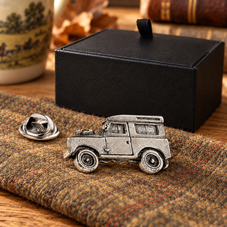 Farley's Land Rover Defender pewter lapel pin badge on tweed beside the black presentation box