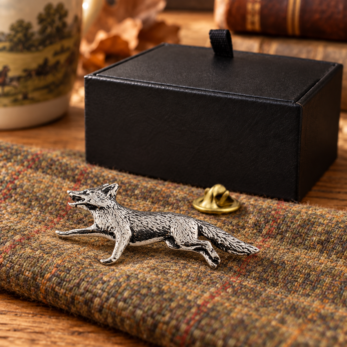Farley's running fox English pewter lapel pin badge on tweed beside the black presentation box