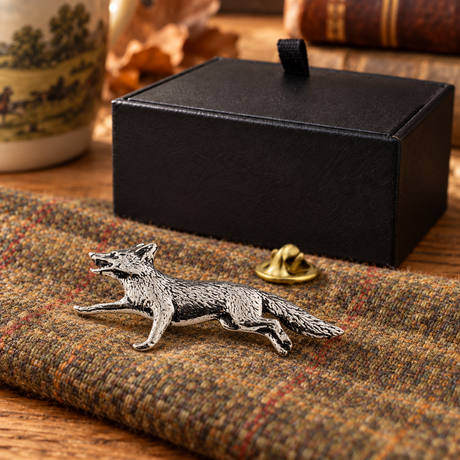 Farley's running fox English pewter lapel pin badge on tweed beside the black presentation box