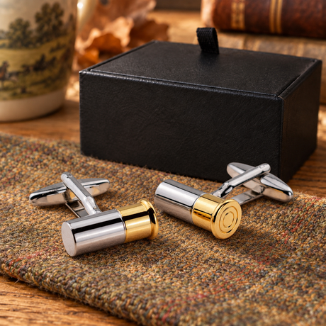 Pair of Farley's two tone shotgun cartridge cufflinks on tweed beside the black presentation box