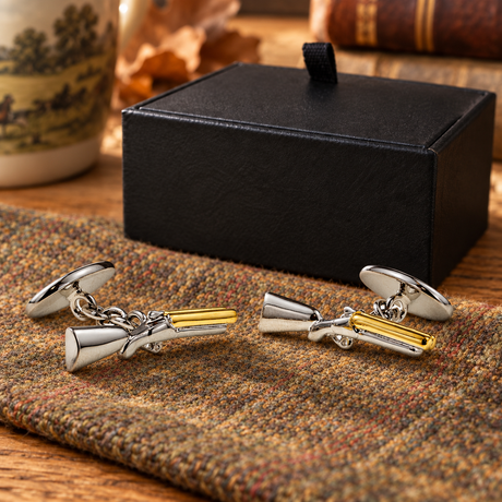 Pair of Farley's two tone shotgun cufflinks with chain fastenings on tweed beside the black presentation box