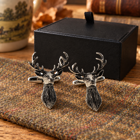 Pair of Farley's stag head English pewter cufflinks on tweed beside the black presentation box
