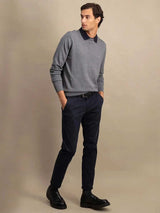 A man modeling a gray long-sleeve polo sweater with a dark navy collar, paired with navy trousers and black leather shoes, against a solid beige studio background.