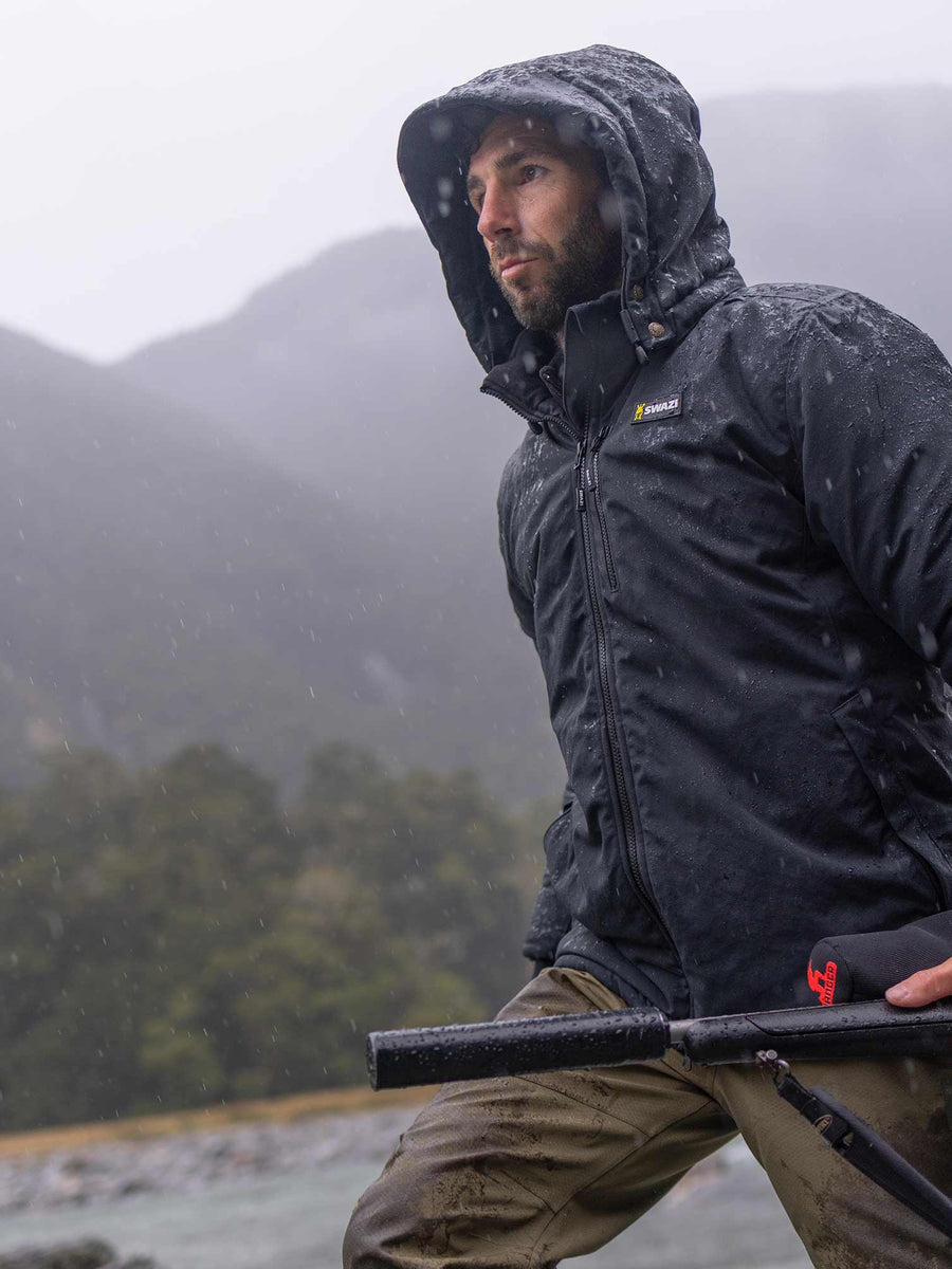 Swazi Geyser Jacket in Black, worn beside a river in wet conditions