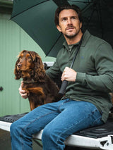 Man sitting on a vehicle's tailgate with a dog, holding an umbrella.