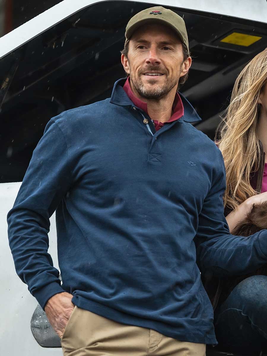 Man wearing a blue pullover and beige cap standing next to a white vehicle.