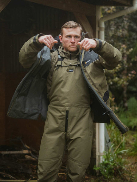 Swazi Torrent Waterproof Jacket in Ranger / Black, worn while putting on the jacket outdoors