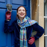 Woman wearing touchscreen single point faux fur lined leather gloves in wine red, in a  blue coat and scarf against a blue door. 