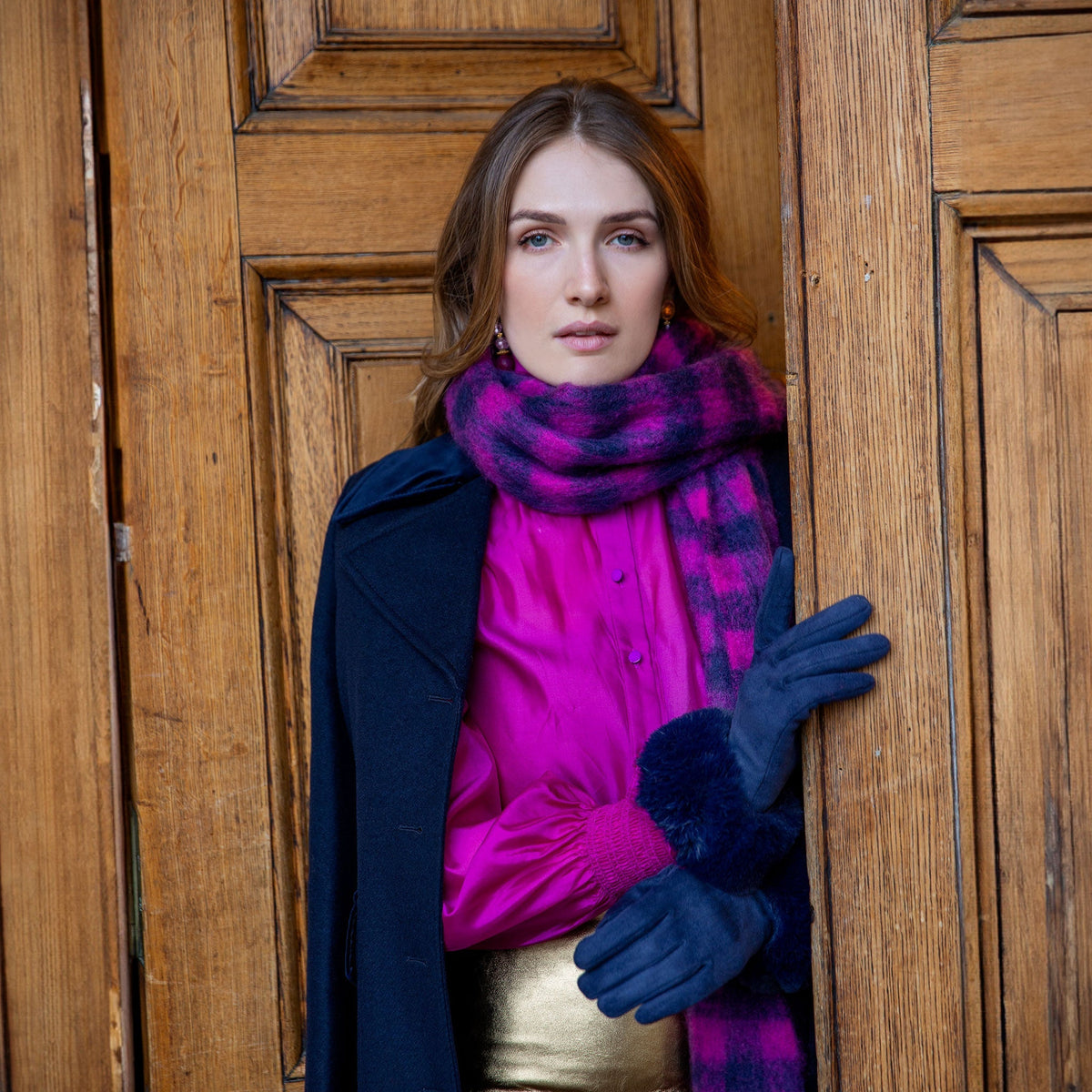Woman wearing Women's touchscreen velour-lined faux suede gloves with faux fur cuffs in navy by a grand door