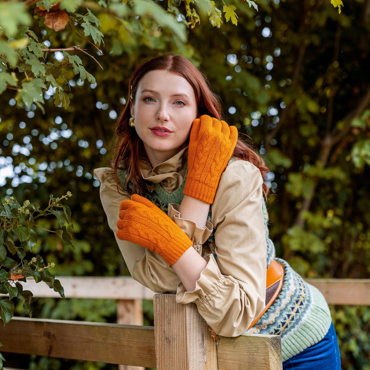 Woman wearing cable knit gloves in pumpkin leaning on a wooden bridge