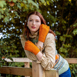 Woman wearing cable knit gloves in pumpkin leaning on a wooden bridge