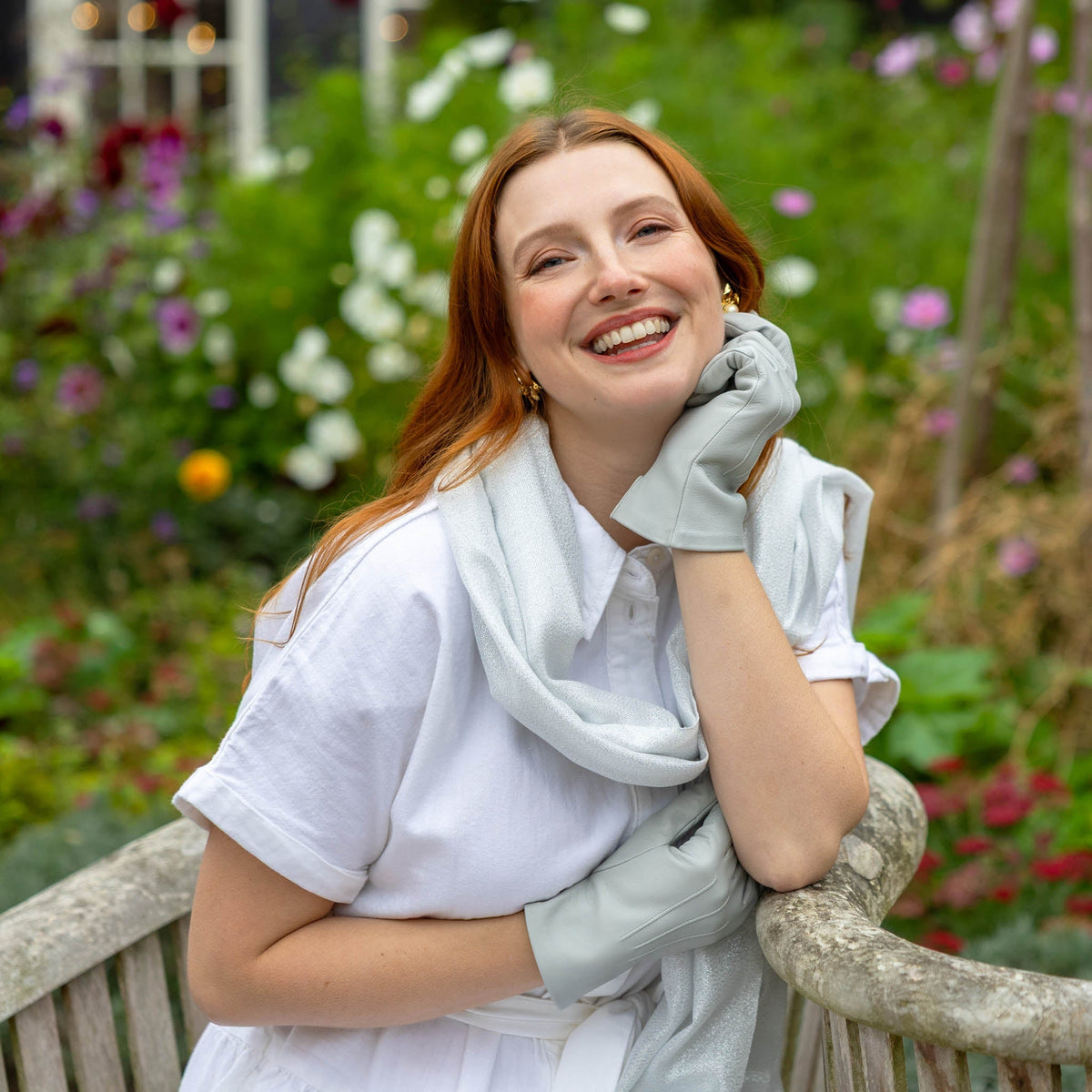 Woman wearing leather gloves in silver sitting on a bench in front of floral garden