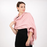 Woman wearing plain pashmina in pale pink in studio. 