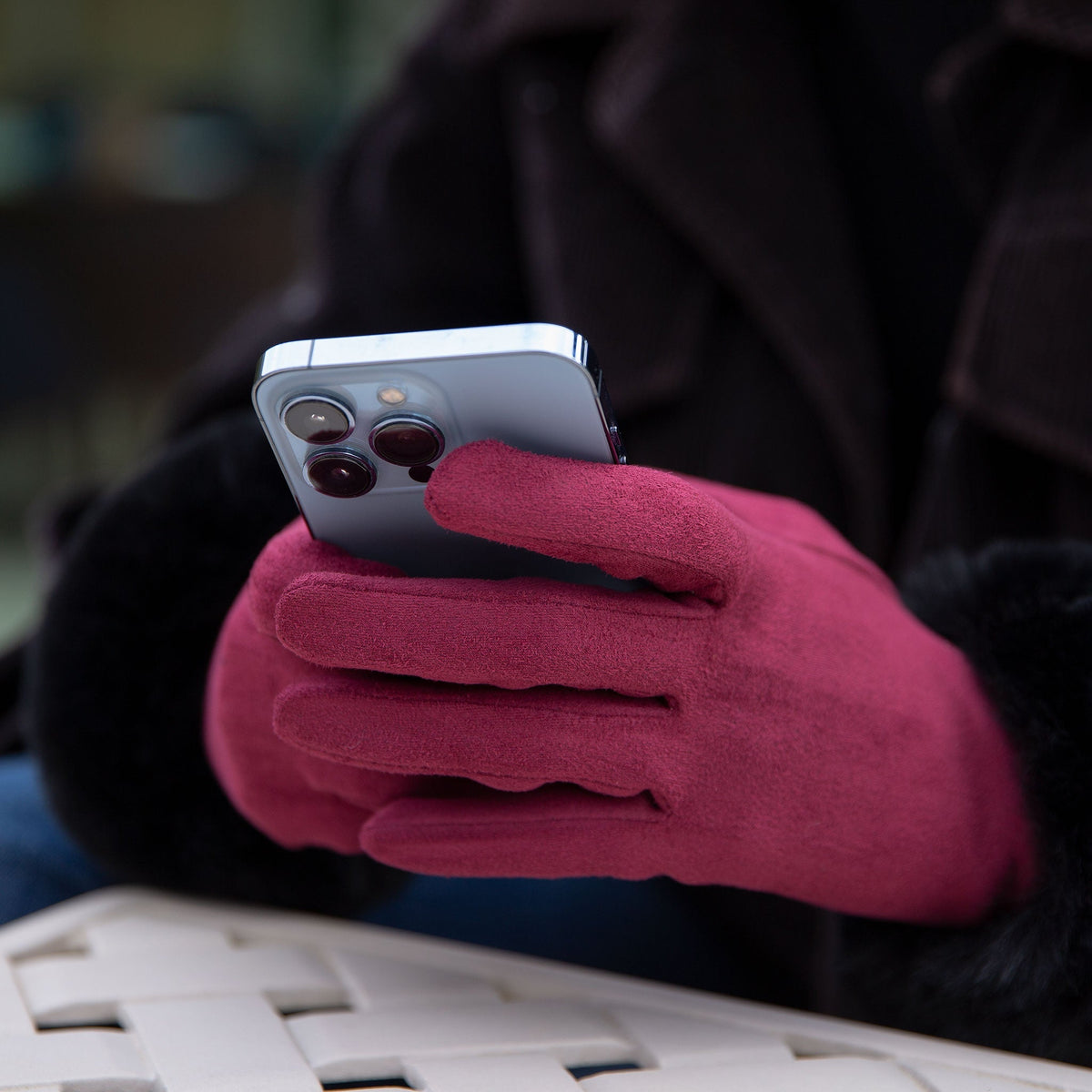 Woman wearing touchscreen faux suede gloves with faux fur cuffs in berry/black whilst using her phone