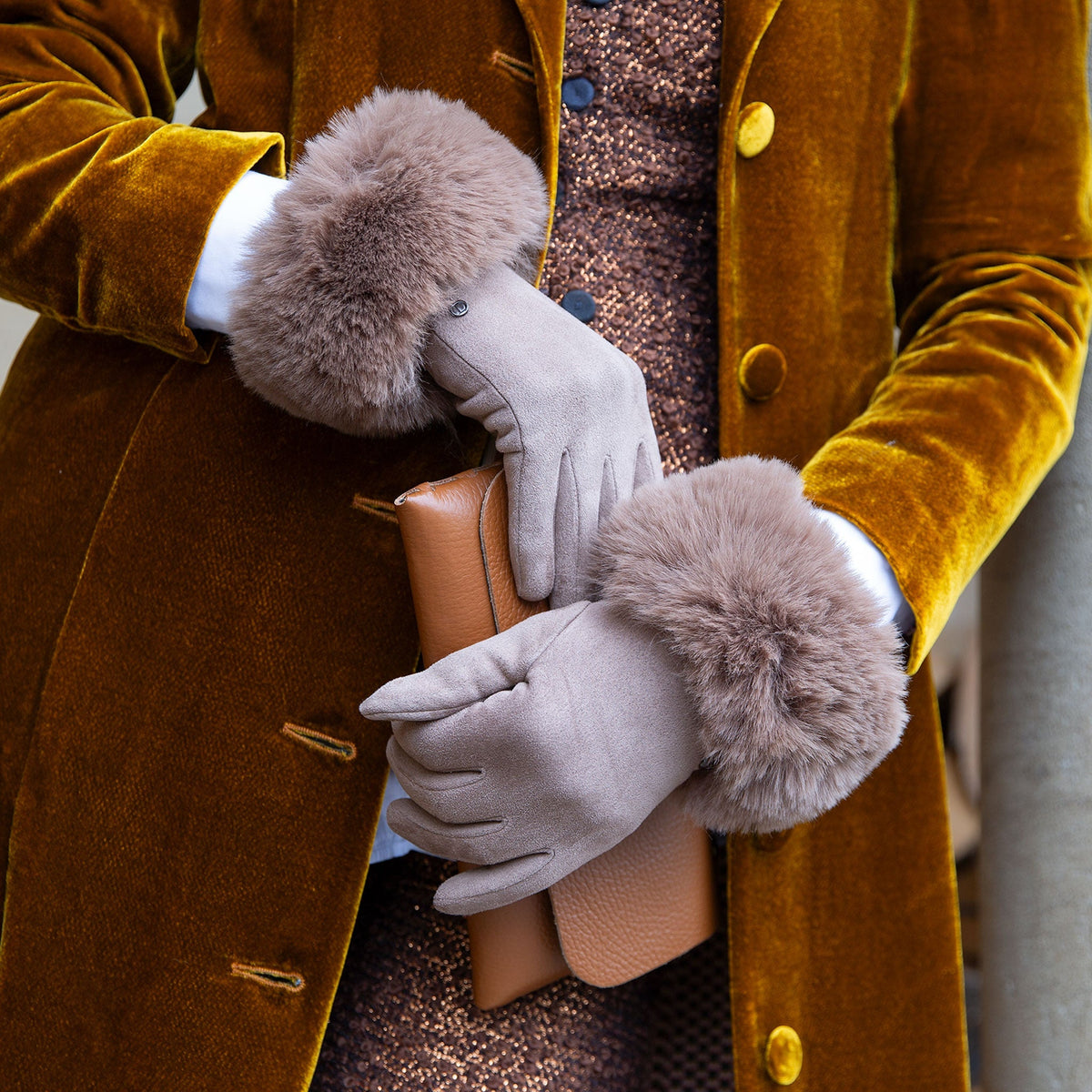 Woman wearing touchscreen velour-lined faux suede gloves with faux fur cuffs in camel at a cafe